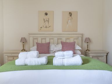 A bedroom with a bed with white linens green blanket and four white towels two bedside tables with lamps and two paintings above the headboard at Crabtree in Hawkshead