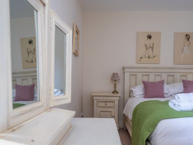 A bedroom with a bed with green throw and pink cushions beside a small wooden nightstand with a lamp at Crabtree in Hawkshead