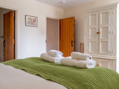 A bedroom with a bed covered by a green bedspread and white towels folded on top a white wardrobe and wooden doors on the wall at Crabtree in Hawkshead