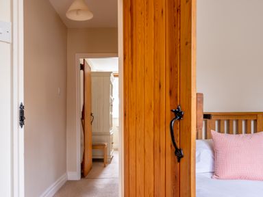 A hallway leading to a room with a wooden wardrobe and chair and a partially visible wooden bed with a pink pillow at Crabtree in Hawkshead
