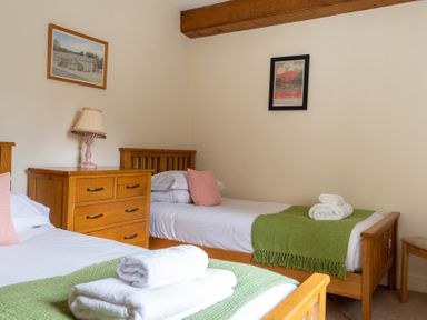 A bedroom with two single wooden beds a wooden chest of drawers with lamp and folded towels on beds at Crabtree in Hawkshead