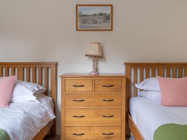 A bedroom with two wooden beds separated by a wooden chest of drawers with a lamp and a framed picture above at Crabtree in Hawkshead