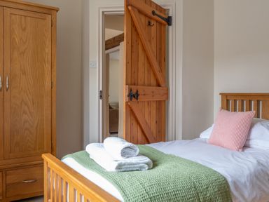 A bedroom with a wooden bed with white sheets and a green blanket a wooden wardrobe and an open wooden door showing another room at Crabtree Hawkshead
