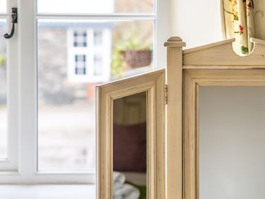 A wooden corner cabinet with a small door open in front of a window with a view outside at Crabtree in Hawkshead