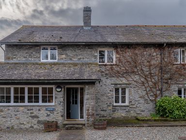 A stone house with windows and a blue door with plants in wooden barrels outside at Crabtree in Hawkshead