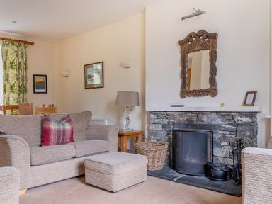 A living room with a sofa ottoman stone fireplace and a wooden framed mirror at Forge in Graythwaite near Hawkshead