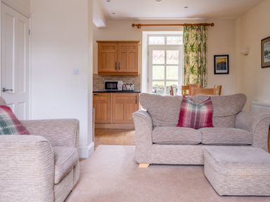 A living room with sofas and plaid cushions next to a kitchen with wooden cabinets and a dining table at Forge in Graythwaite near Hawkshead