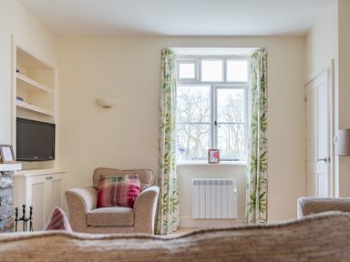 A sitting room with armchairs a window with curtains and a television at Forge in Graythwaite near Hawkshead