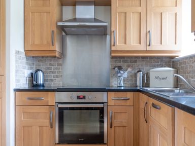 A kitchen with wooden cabinets an electric oven stovetop kettle bread box and utensil holder at Forge in Graythwaite near Hawkshead