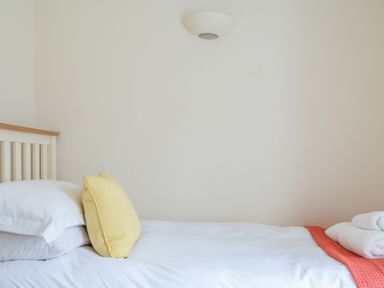 A bed with white sheets a yellow pillow white towels and an orange blanket on a white wall bedroom at Forge in Graythwaite near Hawkshead