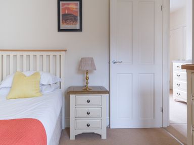 A bedroom with a bed with a yellow pillow a bedside table with a lamp and a white door at Forge in Graythwaite near Hawkshead