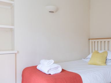 A bedroom with a single bed with white sheets yellow pillow and folded white towels on a red blanket at Forge Graythwaite near Hawkshead