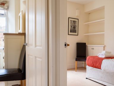 A bedroom with a bed covered with a red blanket and white towels two black chairs white shelves and a cabinet with a framed photograph on the wall at Forge in Graythwaite near Hawkshead