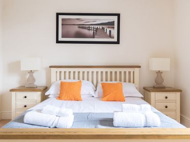 A bedroom with a bed that has orange pillows and folded white towels on it and two bedside tables with lamps and a framed picture above the bed at Forge in Graythwaite near Hawkshead
