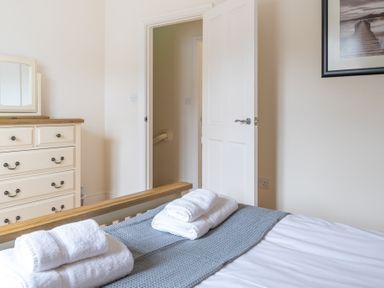 A bedroom with a bed with folded towels a dresser with a mirror an open door and a framed photo on the wall at Forge in Graythwaite near Hawkshead