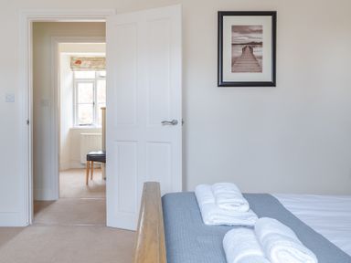 A bedroom with a partially open door showing an adjacent room with a chair near a window and a framed picture on the wall at Forge in Graythwaite near Hawkshead