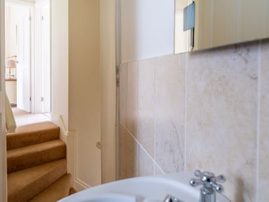 A narrow hallway with carpeted stairs leading to a room with an open door and a sink with tiled walls on the right at Forge Graythwaite near Hawkshead