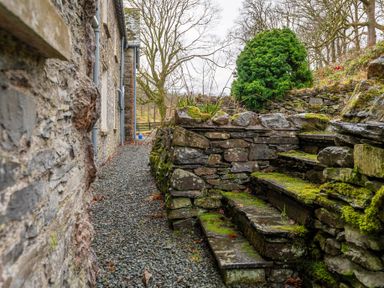 A stone pathway next to a stone building with moss-covered stone steps and trees in the background at Forge in Graythwaite near Hawkshead