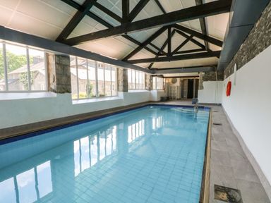 An indoor swimming pool with large windows stone walls and exposed ceiling beams at Newlands in Graythwaite near Hawkshead