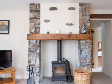 A stone fireplace with a wood stove and a basket in a living room at Newlands in Graythwaite near Hawkshead