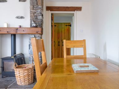Dining area with wooden table and chairs next to a stone fireplace with a wood burning stove and a basket Newlands Graythwaite near Hawkshead
