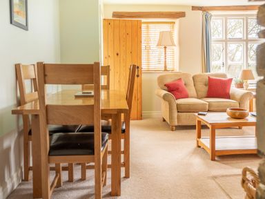 A dining area with wooden table and chairs next to a sitting area with a sofa and coffee table at Newlands in Graythwaite near Hawkshead