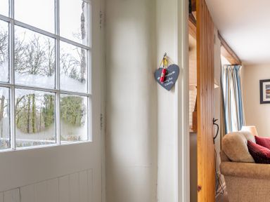 A windowed door with condensation next to a wall with a hanging heart-shaped sign and a partially visible living area at Newlands in Graythwaite near Hawkshead