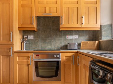 A kitchen with wooden cabinets a stainless steel oven a toaster a wooden bread box and utensils in a container at Newlands Graythwaite near Hawkshead