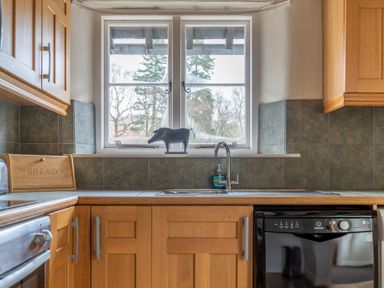 A kitchen with wooden cabinets a window above the sink and a bread box on the countertop at Newlands in Graythwaite near Hawkshead