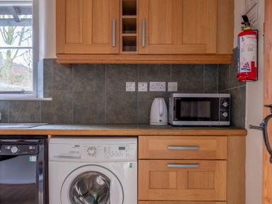 A kitchen counter with a washing machine microwave kettle wooden cabinets and a fire extinguisher at Newlands in Graythwaite near Hawkshead