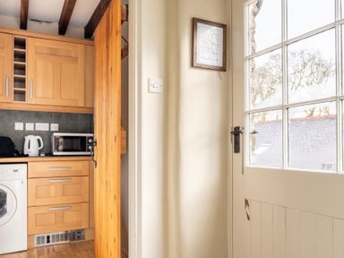 A kitchen area with wooden cabinets a microwave kettle and washing machine next to a white door with glass panes at Newlands Graythwaite near Hawkshead