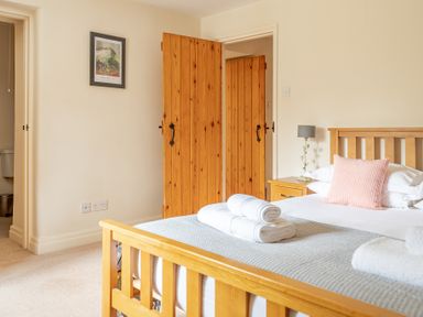 A bedroom with a wooden bed frame towels on the bed and wooden doors at Newlands in Graythwaite near Hawkshead