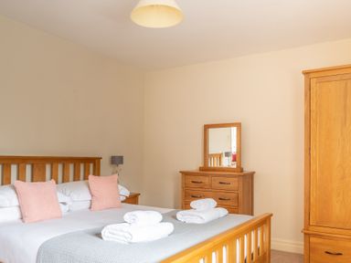 A bedroom with a wooden bed frame and pink cushions alongside a wooden chest of drawers with a mirror and a wooden wardrobe at Newlands Graythwaite near Hawkshead