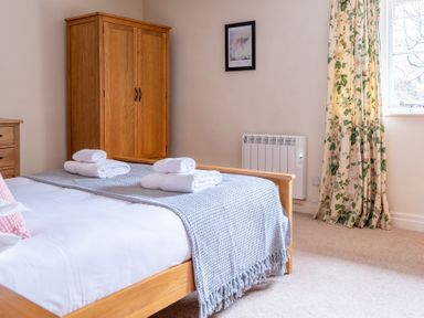 A bedroom with a wooden bed with folded towels on a blanket a wooden wardrobe floral curtains and a window at Newlands Graythwaite near Hawkshead