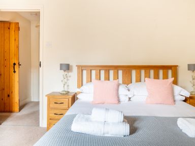 A bedroom with a wooden bed frame two bedside tables with lamps and folded towels on the bed at Newlands Graythwaite near Hawkshead