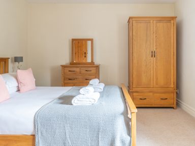 A bedroom with a bed with pink pillows and grey blanket a wooden dresser with mirror and a wooden wardrobe at Newlands in Graythwaite near Hawkshead
