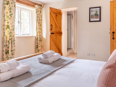 A bedroom with folded towels on a bed wooden door with a lock floral curtains and a framed picture on the wall at Newlands in Graythwaite near Hawkshead