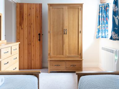 A bedroom with wooden wardrobe dresser beds and window with blue curtains at Newlands in Graythwaite near Hawkshead