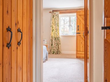 A bedroom with wooden doors a window with floral curtains and a carpeted floor at Newlands in Graythwaite near Hawkshead