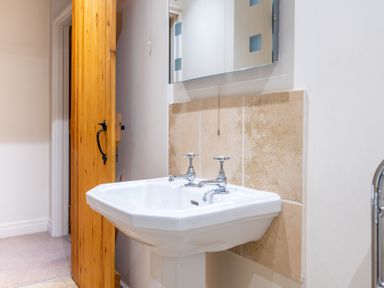A bathroom with a white sink having two taps a wooden door and a mirror above the sink at Newlands in Graythwaite near Hawkshead