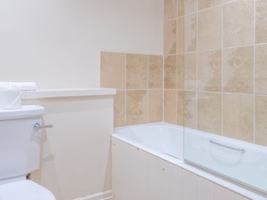 A bathroom with a white toilet and a bathtub with beige tiled walls at Newlands in Graythwaite near Hawkshead