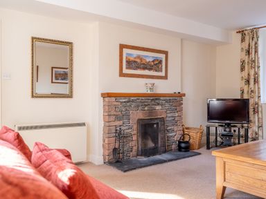 A living room with a stone fireplace a television on a stand and a red sofa at Greenhowes Graythwaite near Hawkshead