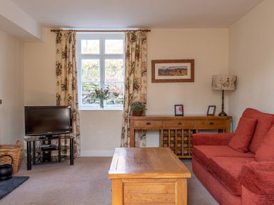 A living room with a red sofa wooden coffee table TV and floral curtains at Greenhowes in Graythwaite near Hawkshead