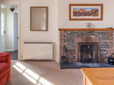 A living room corner with a stone fireplace a framed picture above a wooden mantel a mirror and a red sofa at Greenhowes Graythwaite near Hawkshead