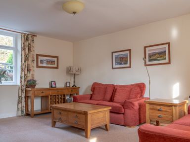 A living room with red sofas wooden coffee table wooden side table and framed pictures on walls at Greenhowes Graythwaite near Hawkshead