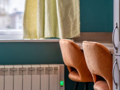 Orange chairs at a wooden desk below a window with yellow curtains and a radiator at Greenhowes in Graythwaite near Hawkshead