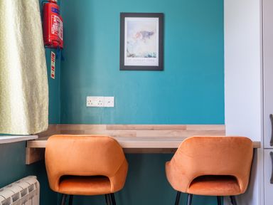 A desk with two orange chairs under a framed picture and fire extinguisher on a turquoise wall at Greenhowes in Graythwaite near Hawkshead