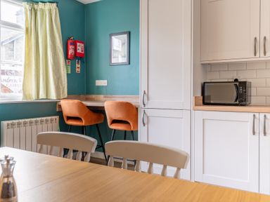 A kitchen with white cabinets a wooden table with chairs two orange bar stools and a microwave at Greenhowes in Graythwaite near Hawkshead