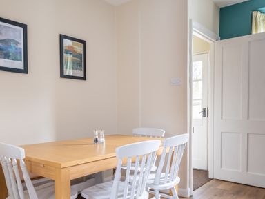 A dining area with a wooden table and white chairs and framed pictures on the wall at Greenhowes Graythwaite near Hawkshead