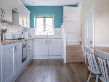 A kitchen with white cabinets and appliances next to a staircase and dining table with chairs at Greenhowes in Graythwaite near Hawkshead